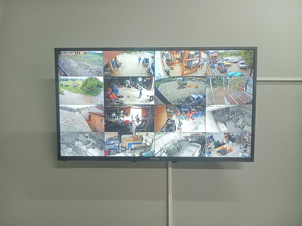 Wall-mounted monitor showing sixteen camera views of a farm yard, workshops and stores