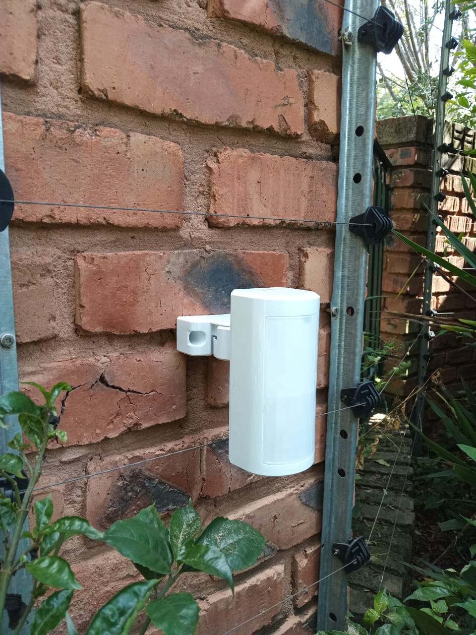 Outdoor motion detector on a brick wall beside electric fence wires