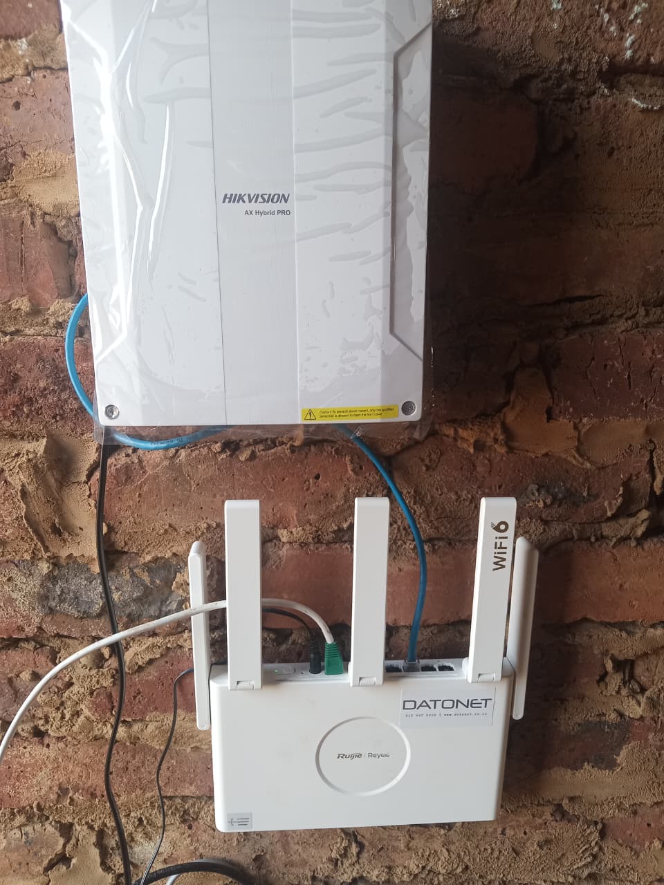 Hikvision AX Hybrid PRO alarm panel mounted above a network router